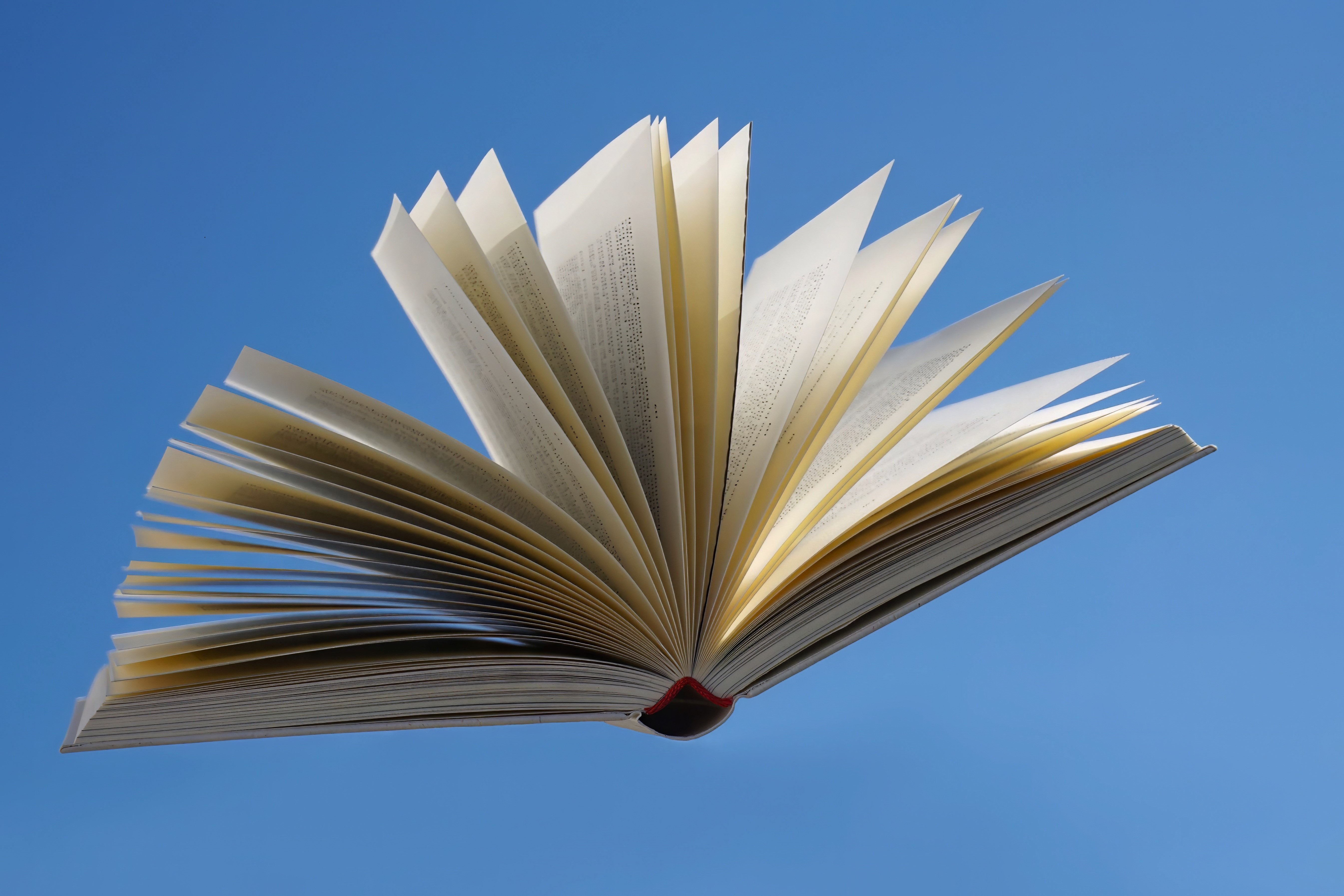 An open book with pages fanned against a blue sky
